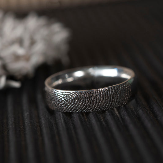 Silver fingerprint ring on a textured dark surface
