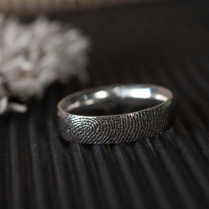 Silver fingerprint ring on a textured dark surface