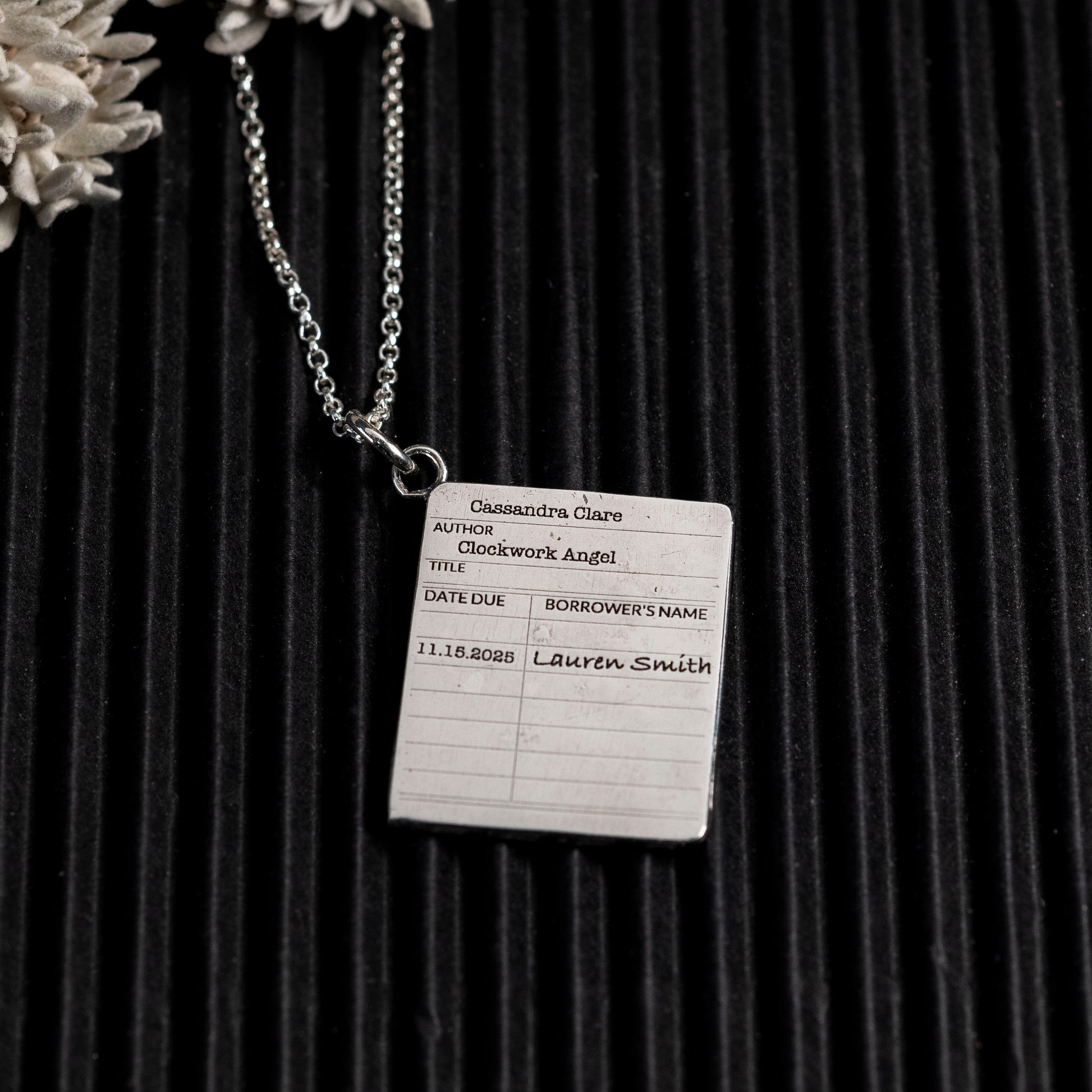 Bookplate necklace with 'Clockwork Angel' by Cassandra Clare on a dark background