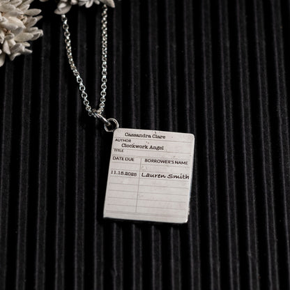 Bookplate necklace with 'Clockwork Angel' by Cassandra Clare on a dark background