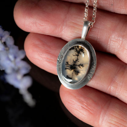Detail of Silver pendant with a black dendritic pattern held in a hand against a dark background