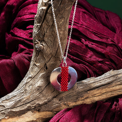 Necklace with a red and silver pendant on a wooden branch against a red fabric background