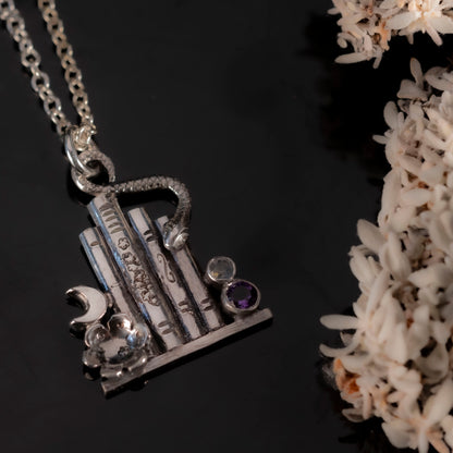 The Midnight Library Necklace in sterling silver featuring a miniature bookshelf with a snake, flower, and faceted stones