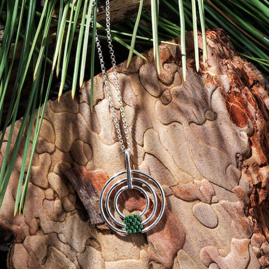 Silver necklace with a green pendant hanging on a textured stone surface with grass in the background