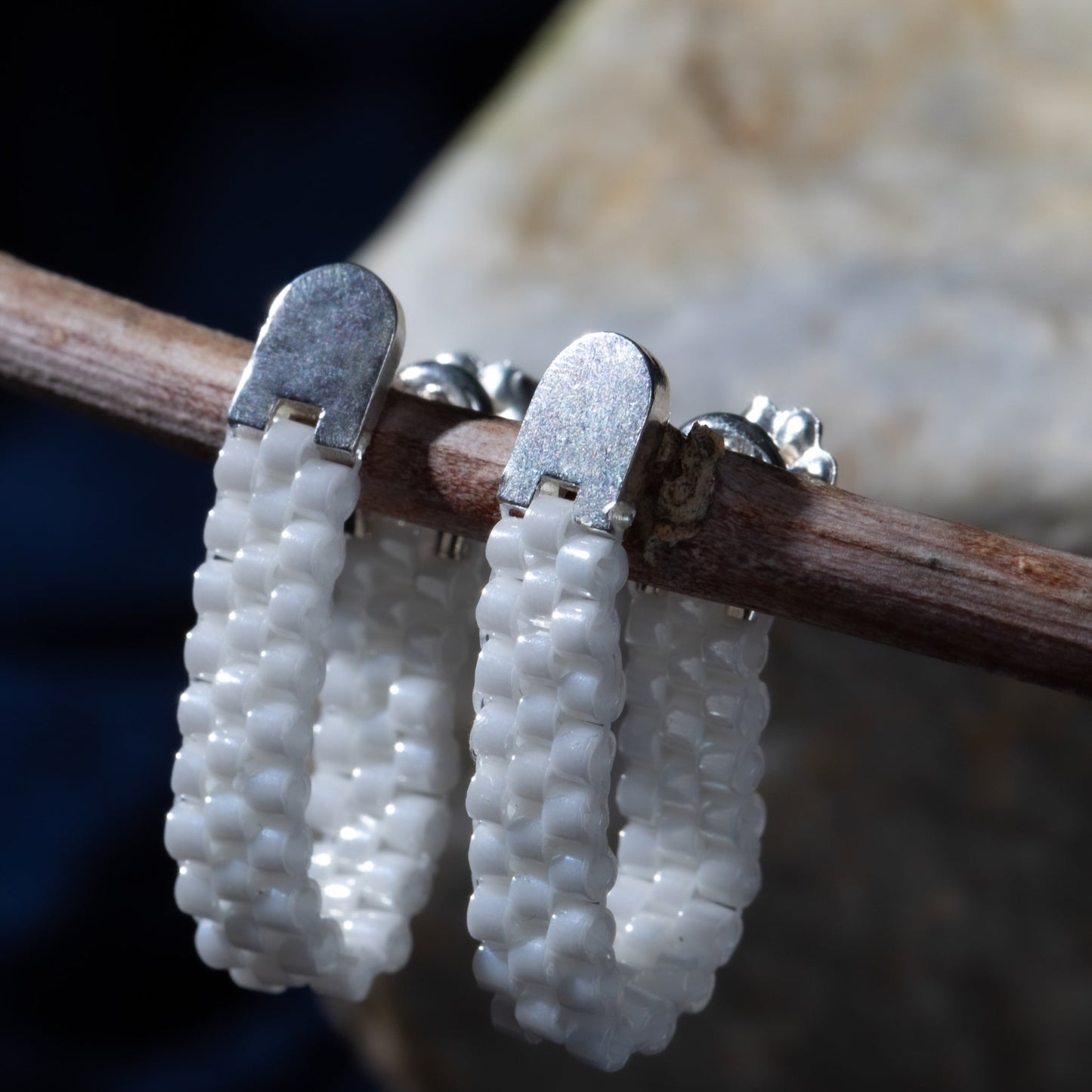 Pair of white beaded earrings on a branch with a blurred natural background