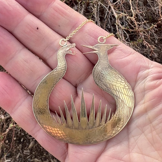 Close-up of the brass Haymitch's Flint Striker pendant showing the snake and mockingbird texture