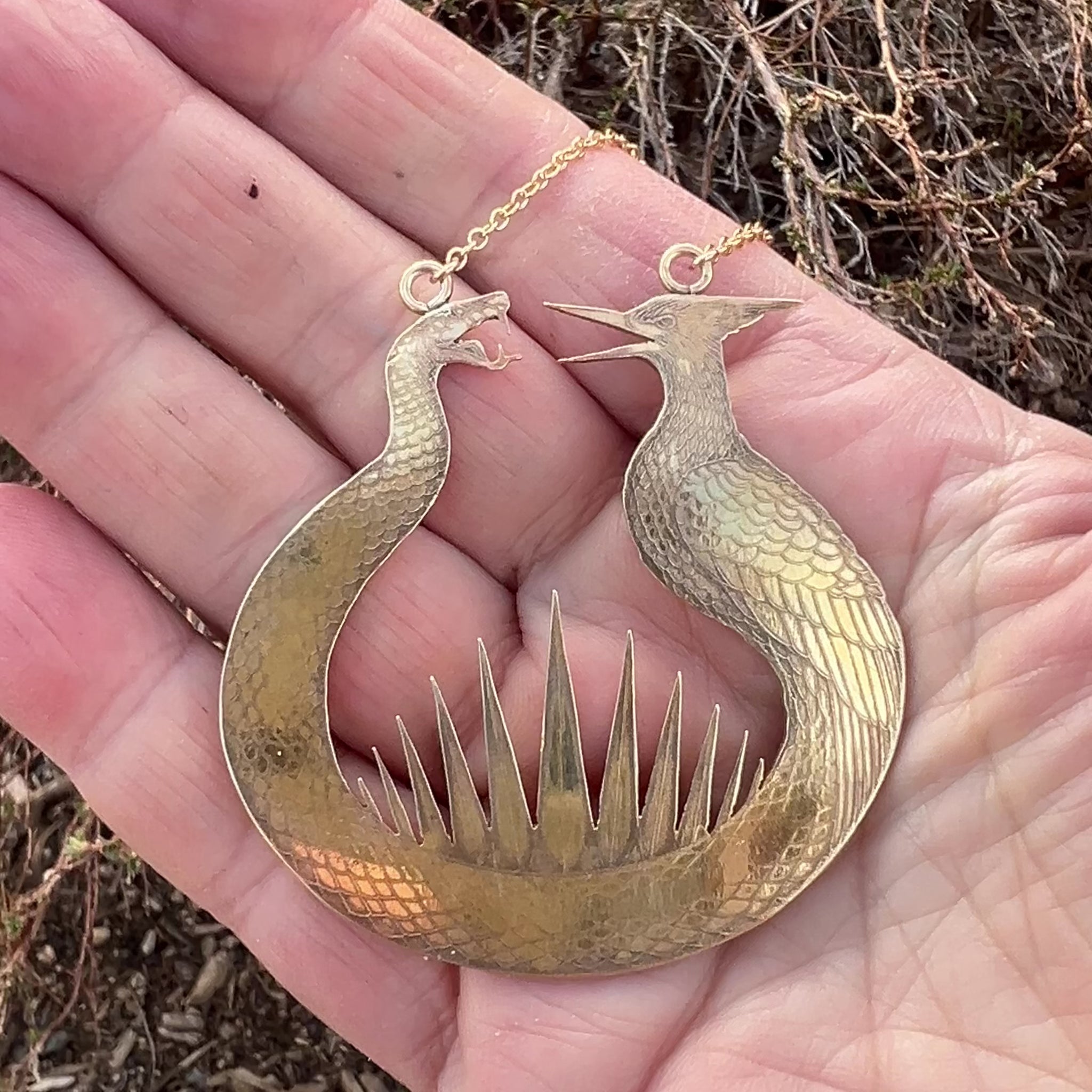 Close-up of the brass Haymitch's Flint Striker pendant showing the snake and mockingbird texture